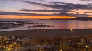 Un puerto deportivo con barcos amarrados, un muelle que se adentra en el agua y una zona de playa con coches estacionados.