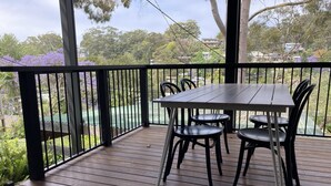 Um deck de madeira com mesa e cadeiras, cercado por um corrimão preto.