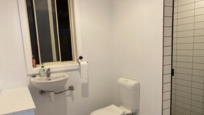 Casa de banho pequena e limpa, com uma sanita branca, lavatório e janela sobre o lavatório.