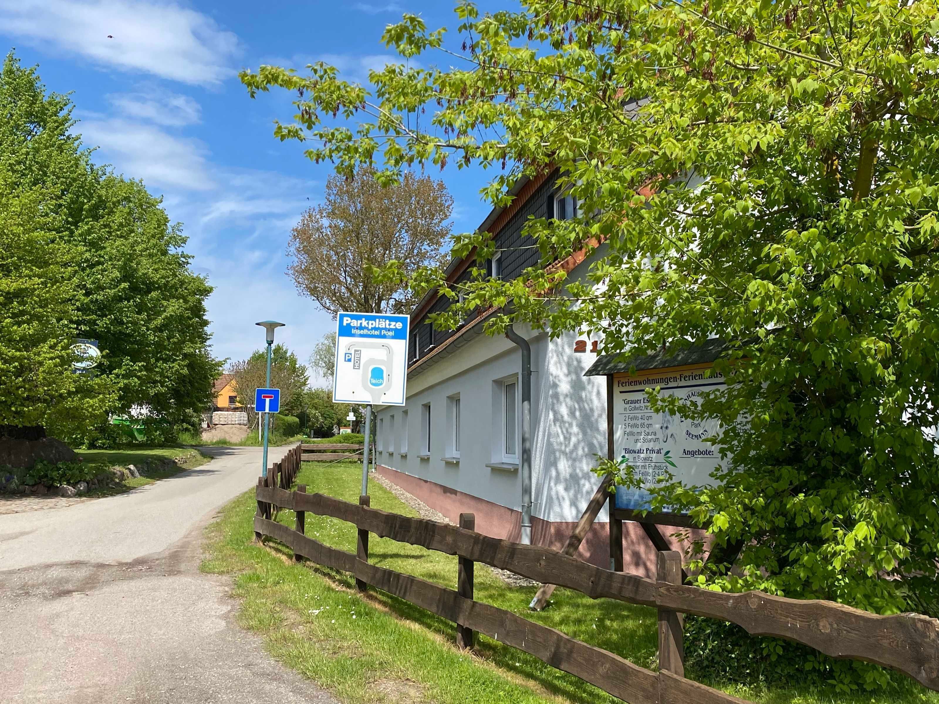 A sign for a hotel with a parking area, a wooden fence, and greenery.