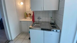 Cozinha compacta com armários brancos, pia de aço inoxidável e fogão embutido.
