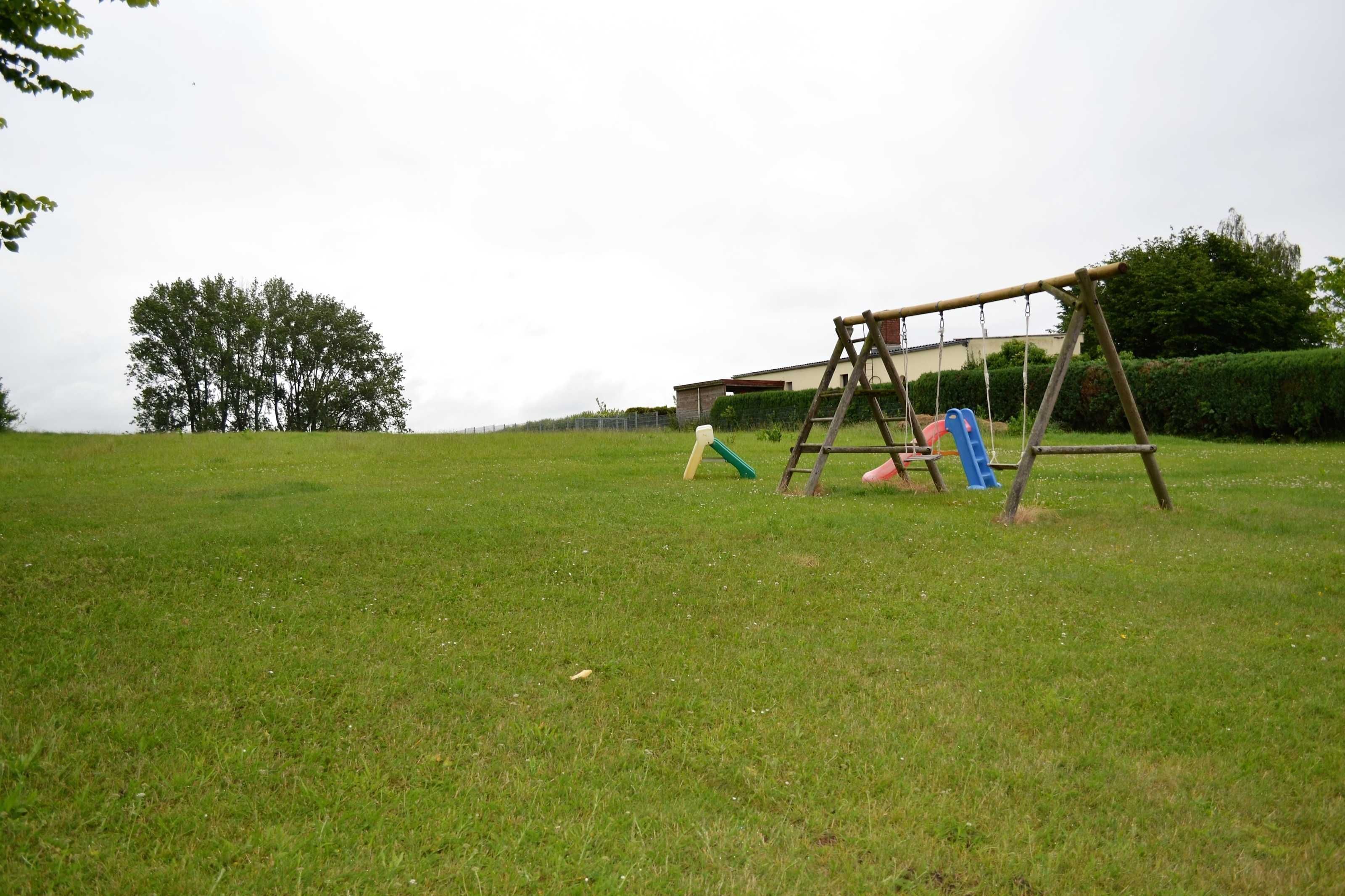 Eine grüne Wiese mit einer Holzschaukel und einer kleinen Spielkonstruktion.