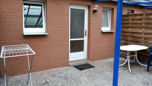 A brick building with a white door, a window, a metal drying rack, and a small white table.