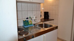 A kitchen with white cabinets, a stainless steel sink, a coffee maker, and a bottle of dish soap.