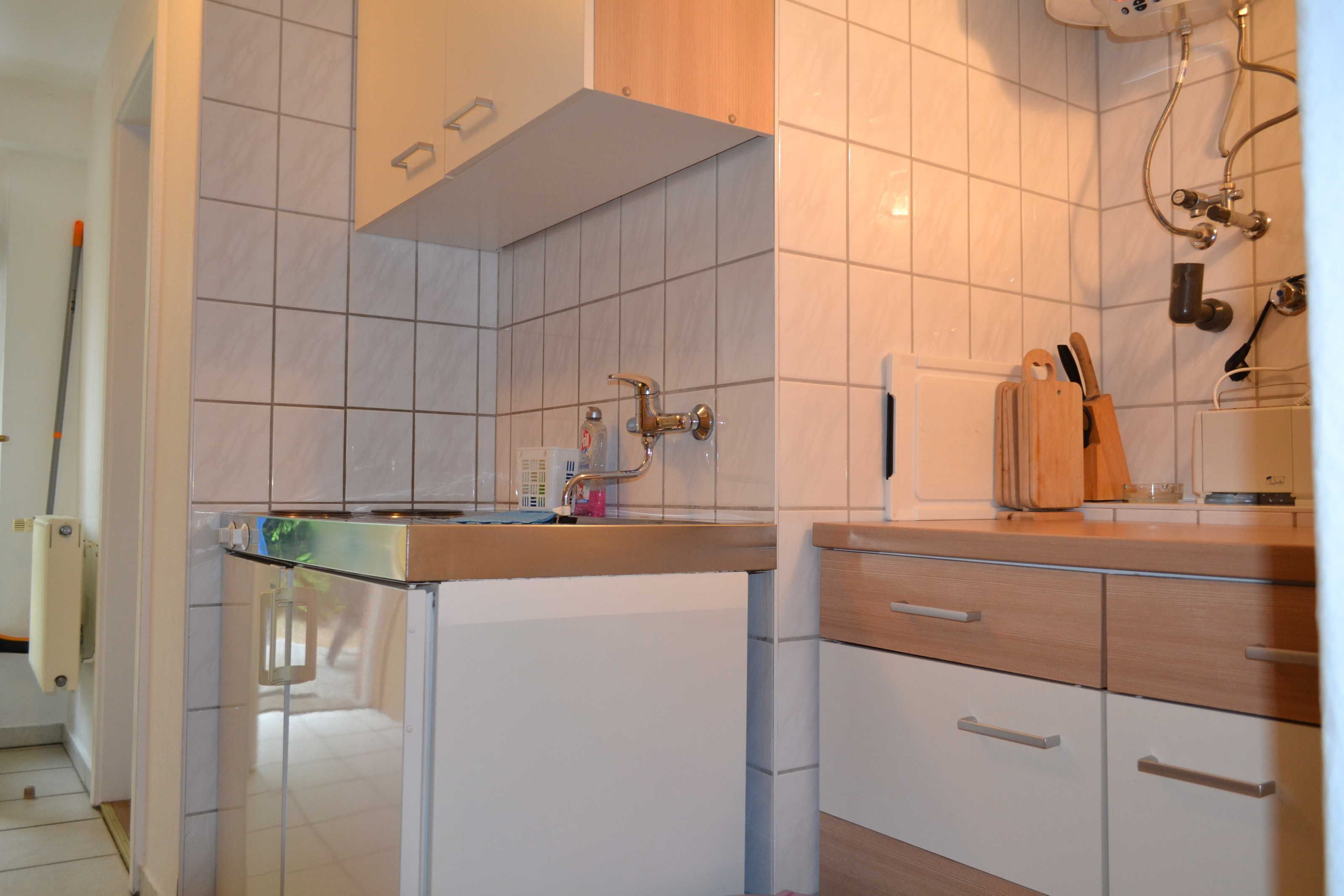 Ett kök med en arbetsbänk i rostfritt stål, vita skåp och en skärbräda i trä.
