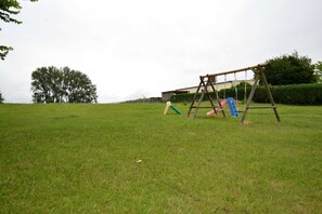 Un campo cubierto de césped con un columpio de madera y una pequeña estructura de juegos.