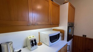 A compact kitchen with wooden cabinets, a microwave, a toaster, and a kettle.