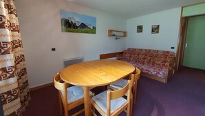 A room with a round wooden table, two chairs, a sofa, and a radiator.