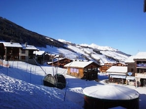 A snow-covered mountain village with wooden buildings, a ski lift, and a clear blue sky.