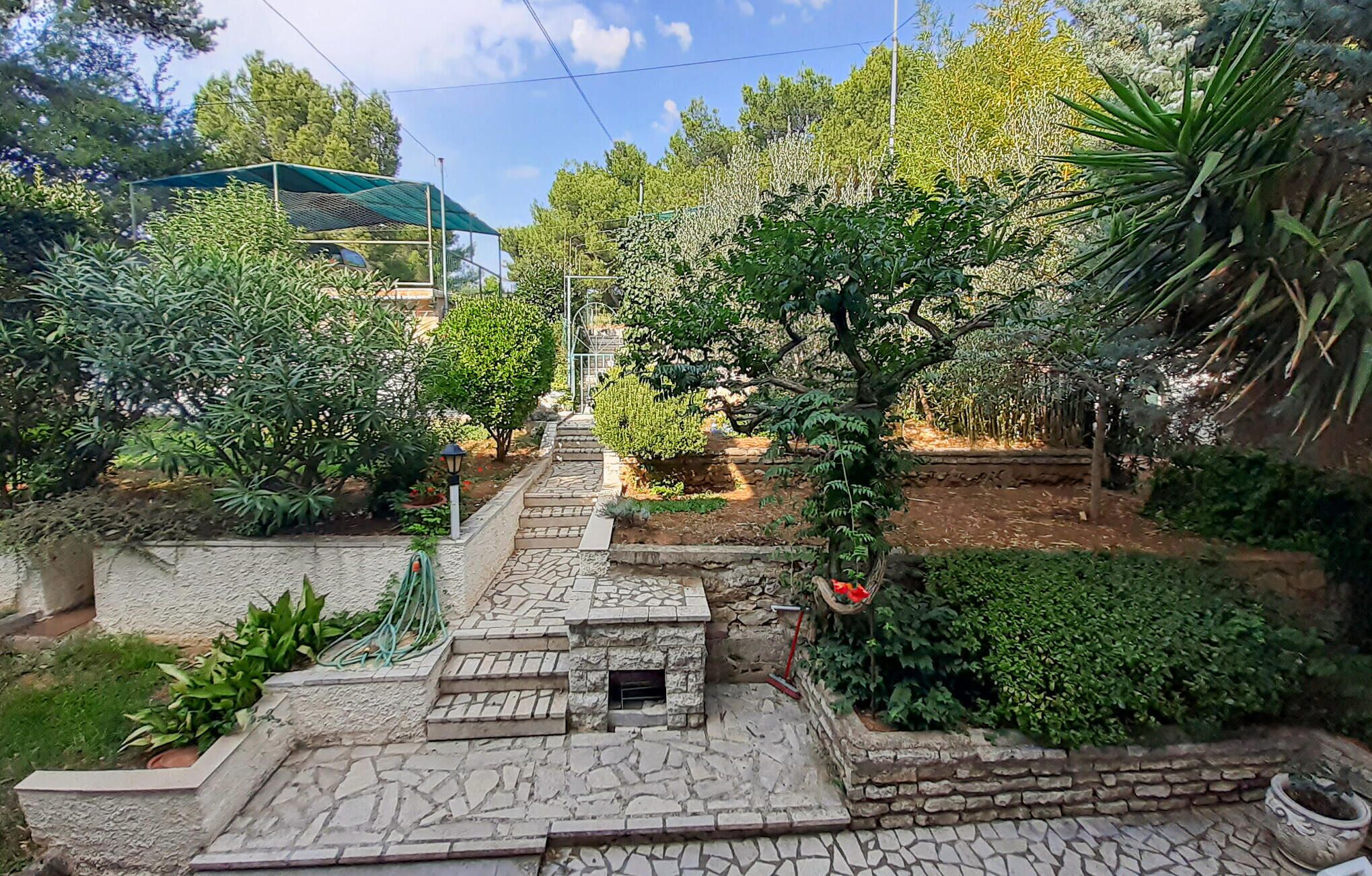 A stone pathway leading up a hill with a small stone structure at the top, surrounded by various plants and trees.