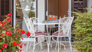Une terrasse avec une table ronde et quatre chaises blanches dotées de coussins rouges. On peut voir deux verres contenant une boisson orange sur la table.