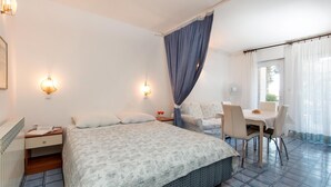 Une chambre d’hôtel avec un lit, un bureau et une chaise. On y trouve deux tables de chevet et une fenêtre avec des rideaux.