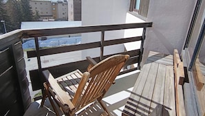 Une terrasse en bois avec une chaise en bois, une rambarde et une vue sur un bâtiment, avec une montagne enneigée en arrière-plan.