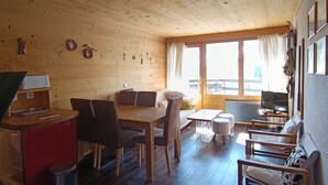 L’intérieur chaleureux d’un chalet avec une table à manger en bois, des chaises, un canapé et un téléviseur.