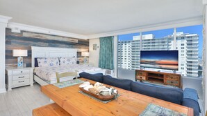 Ein modernes Schlafzimmer mit einem großen Bett, einem Holztisch und Blick auf eine Stadtlandschaft durch große Fenster.