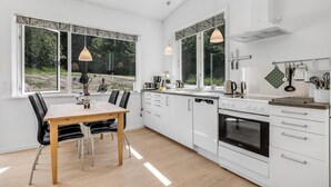 Une cuisine moderne avec des meubles blancs, une table à manger en bois et des luminaires suspendus.