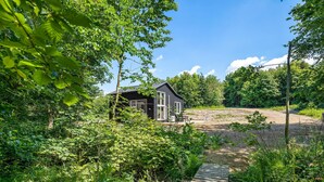 Une cabane entourée d’une végétation luxuriante, accessible par un sentier de terre.