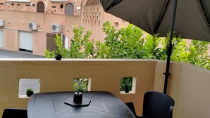 Een balkon met een tafel, stoelen, een grote parasol en potplanten.