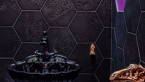 Een badkamer met een wand betegeld met zwarte hexagontegels, een ronde spiegel, een zwart wastafelmeubel met een kraan, en een decoratief object in de vorm van een paardenhoofd.