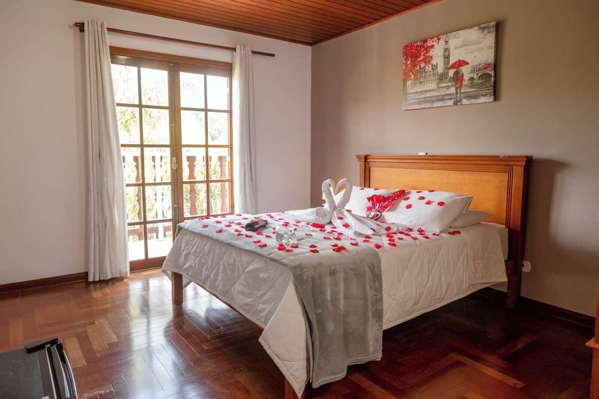 Una cama bien hecha adornada con pétalos de rosa y una botella, un cabecero de madera y un cuadro que muestra a una pareja en un puente.