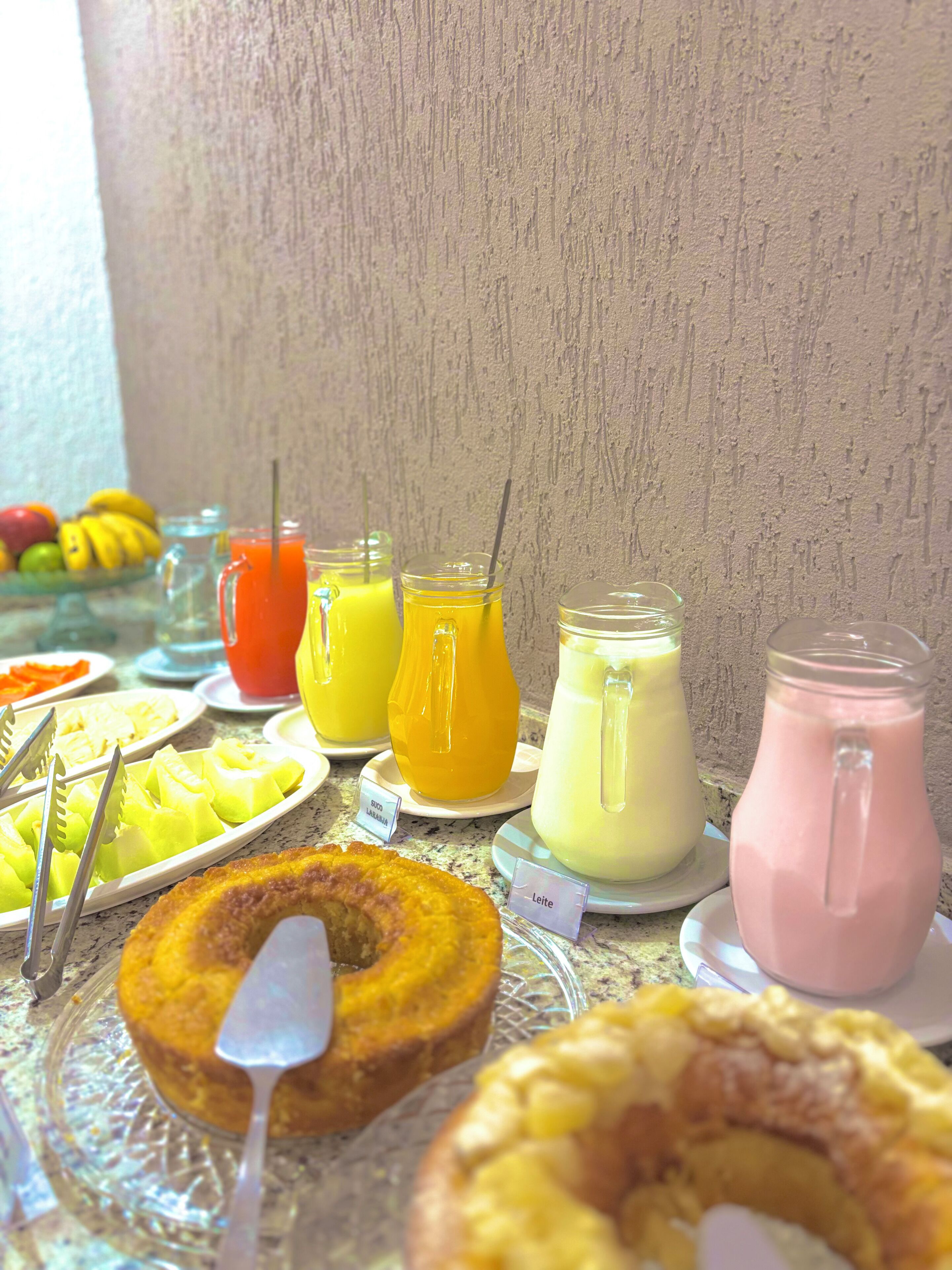 A breakfast buffet with various fruit platters, a cake, and different types of beverages.