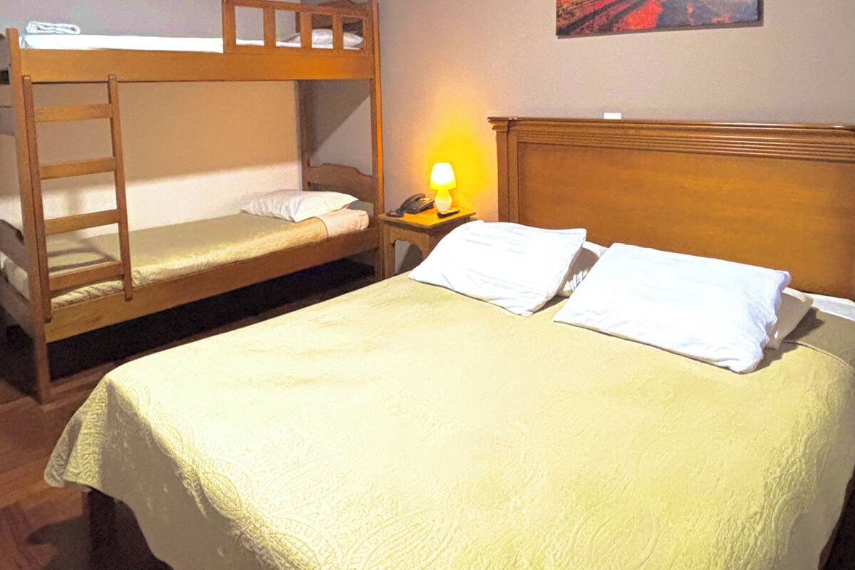 Una habitación con dos literas, una mesita de noche con lámpara y un cuadro en la pared.
