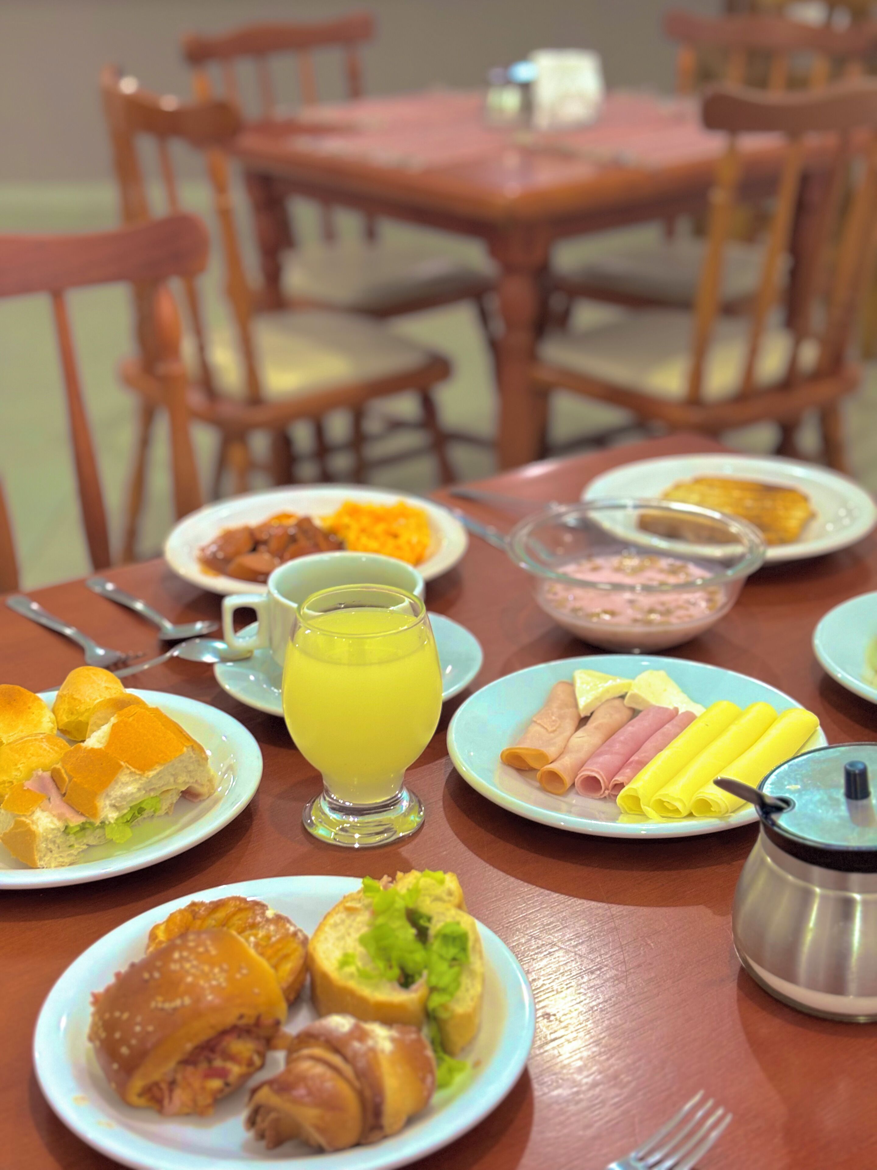 Uma mesa de café da manhã com pratos de comida, um copo de suco de laranja e uma garrafa térmica.