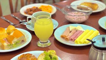 Uma mesa de café da manhã com pratos de comida, um copo de suco de laranja e uma garrafa térmica.