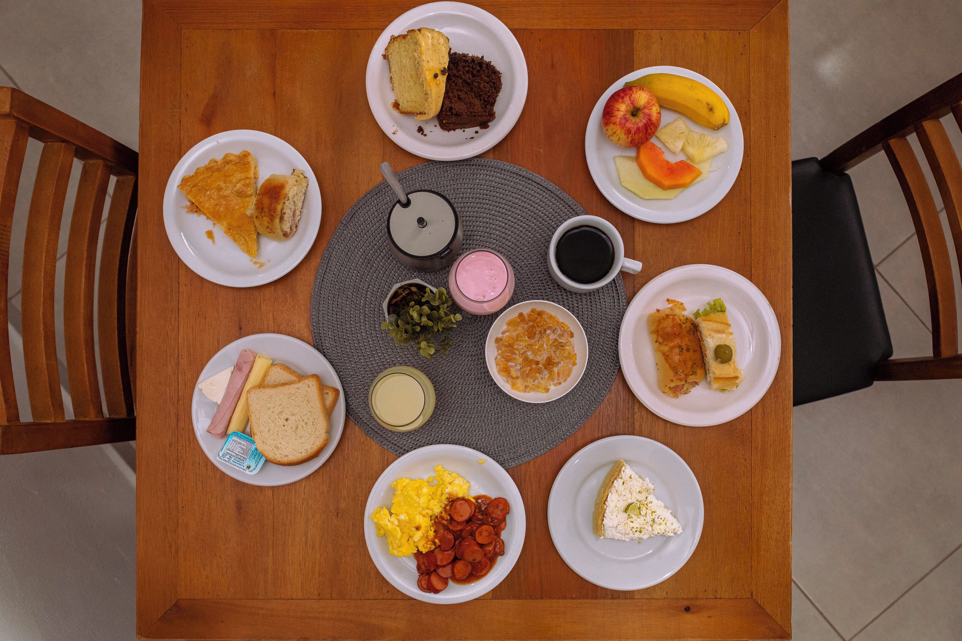 A round wooden table with various plates of food, including sandwiches, fruits, and a cup of coffee.
