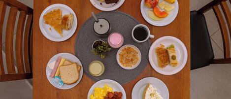 A round wooden table with various plates of food, including sandwiches, fruits, and a cup of coffee.