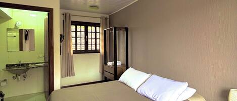 A bedroom with a bed, wooden nightstand, and a bathroom visible through an open door.