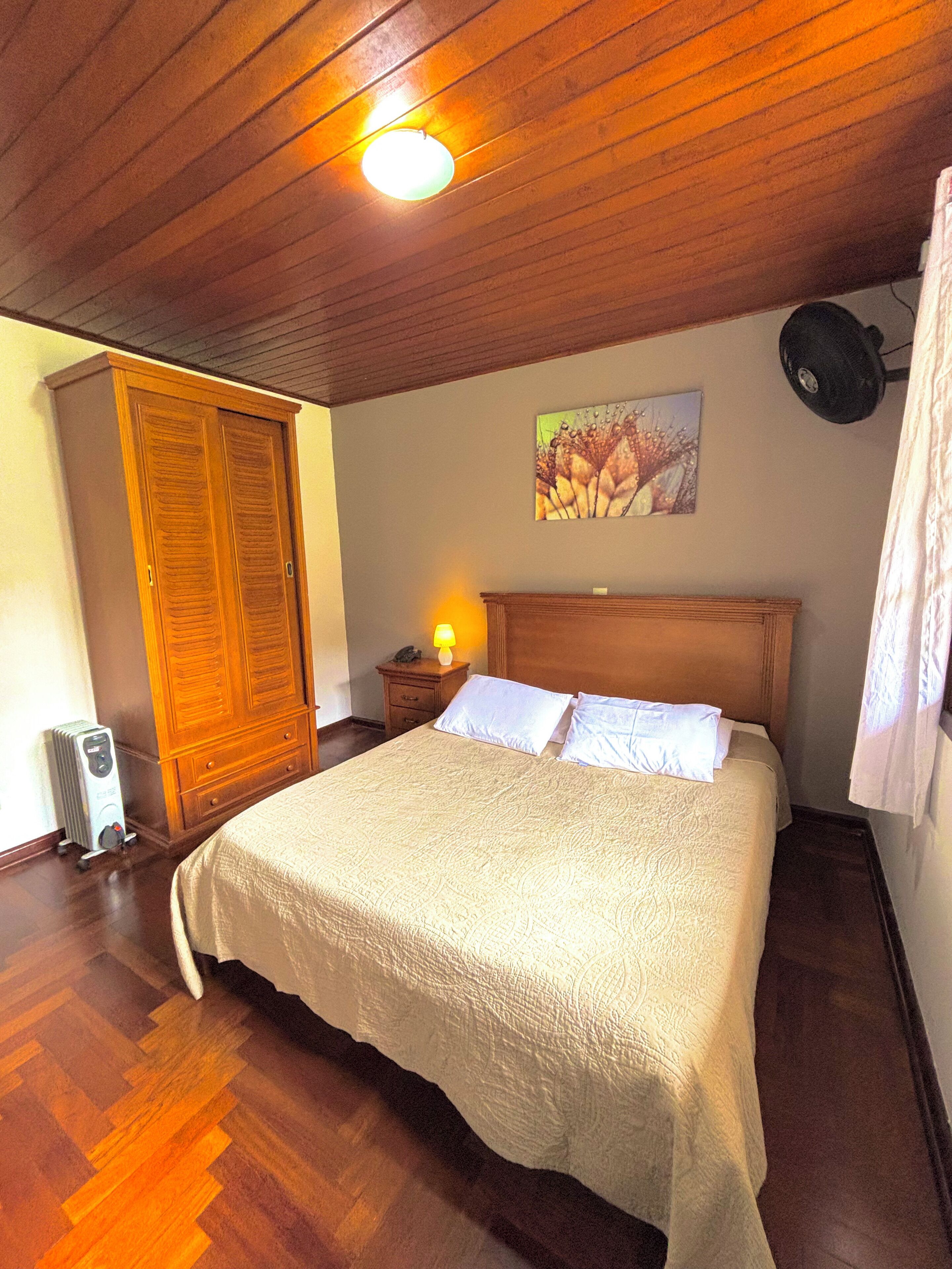 Une chambre avec un plafond en bois, un lit avec une literie blanche, une table de chevet avec une lampe et un tableau au mur.