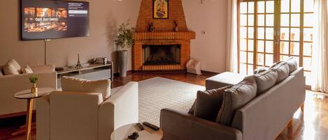 A living room with a fireplace, a television mounted on the wall, and a large window with curtains.
