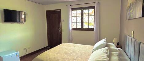 Quarto com cama, televisão, janela com cortinas e porta.