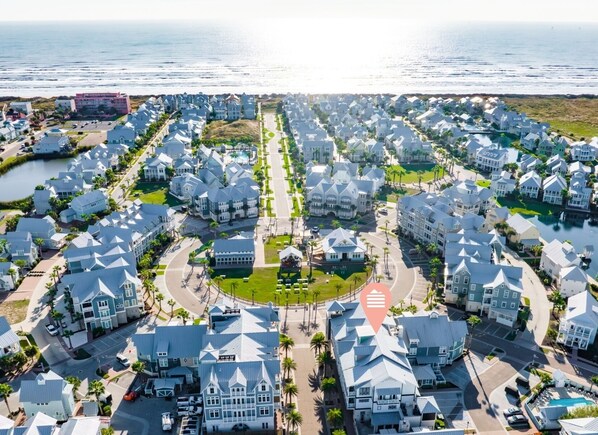 A coastal residential area with uniform houses, a central road, and a body of water in the background. - Luxe, 4-Story Penthouse@Cinnamon Shore near Town Center & More Amenities! (Port Aransas)