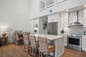 A modern kitchen with white cabinetry, a stainless steel refrigerator, an oven, and a dining area with wicker chairs and a wooden table.