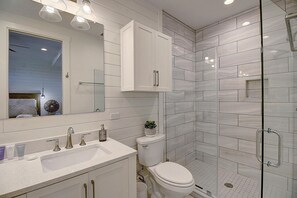 A modern bathroom with a white sink, mirror, and toilet. It features a glass shower enclosure and a small potted plant on the sink. - Luxe, 4-Story Penthouse@Cinnamon Shore near Town Center & More Amenities! (Port Aransas)