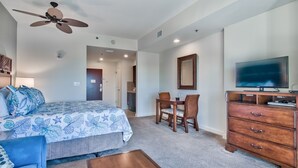 Ein Schlafzimmer mit Bett, Schreibtisch, Fernseher und Deckenventilator.