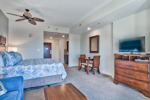 A bedroom with a bed, a desk, a television, and a ceiling fan.