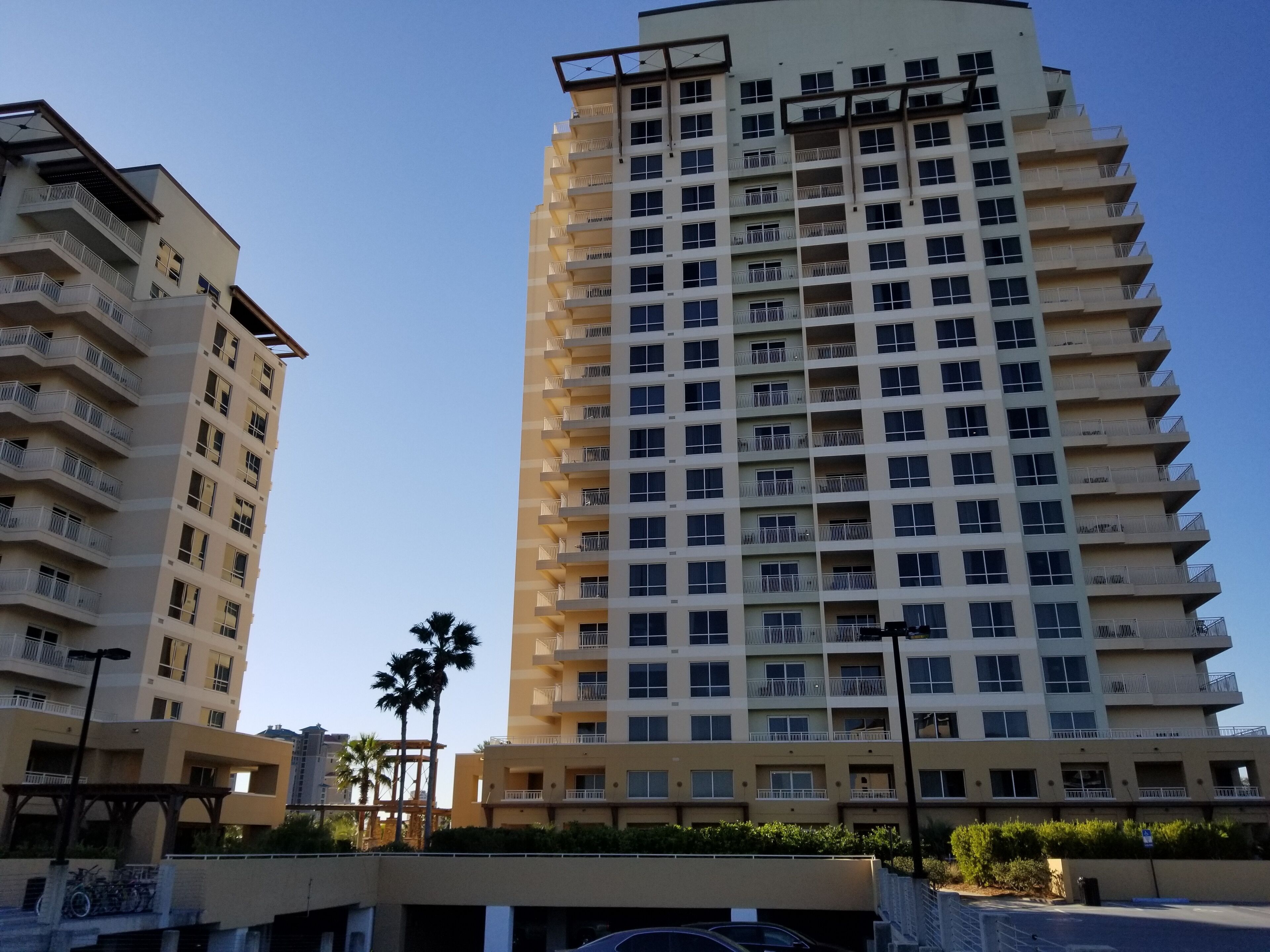 A high-rise residential building with multiple balconies, a flat roof, and a clear sky.