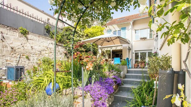 Un jardín con diversas plantas y flores, una silla azul y un paraguas blanco.