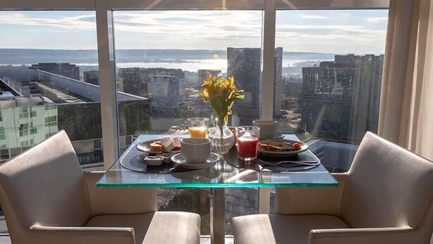 A dining table with a glass top, two chairs, and a vase of flowers. The table is set with plates, cups, and a glass of orange juice. - Flat Saint Moritz - Centro de Brasília (Brasília)