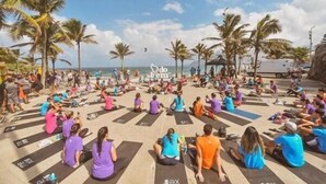 A group of people sitting on yoga mats in a circular formation outdoors, with palm trees and a clear sky in the background. - Flat Saint Moritz - Centro de Brasília (Brasília)