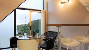 Un espace repas moderne avec une table en verre, des chaises noires et blanches, et une vue sur la verdure environnante.