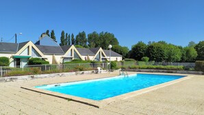 Un espace piscine avec une piscine à l’eau d’un bleu limpide, une clôture blanche et, au fond, un bâtiment doté d’un toit en pente.