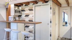 Une cuisine compacte équipée d’un four à micro-ondes, d’une machine à café et de deux tabourets de bar blancs.