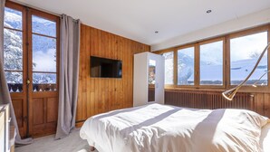 A bedroom with a bed, wooden walls, a TV, and a view of a snowy landscape.