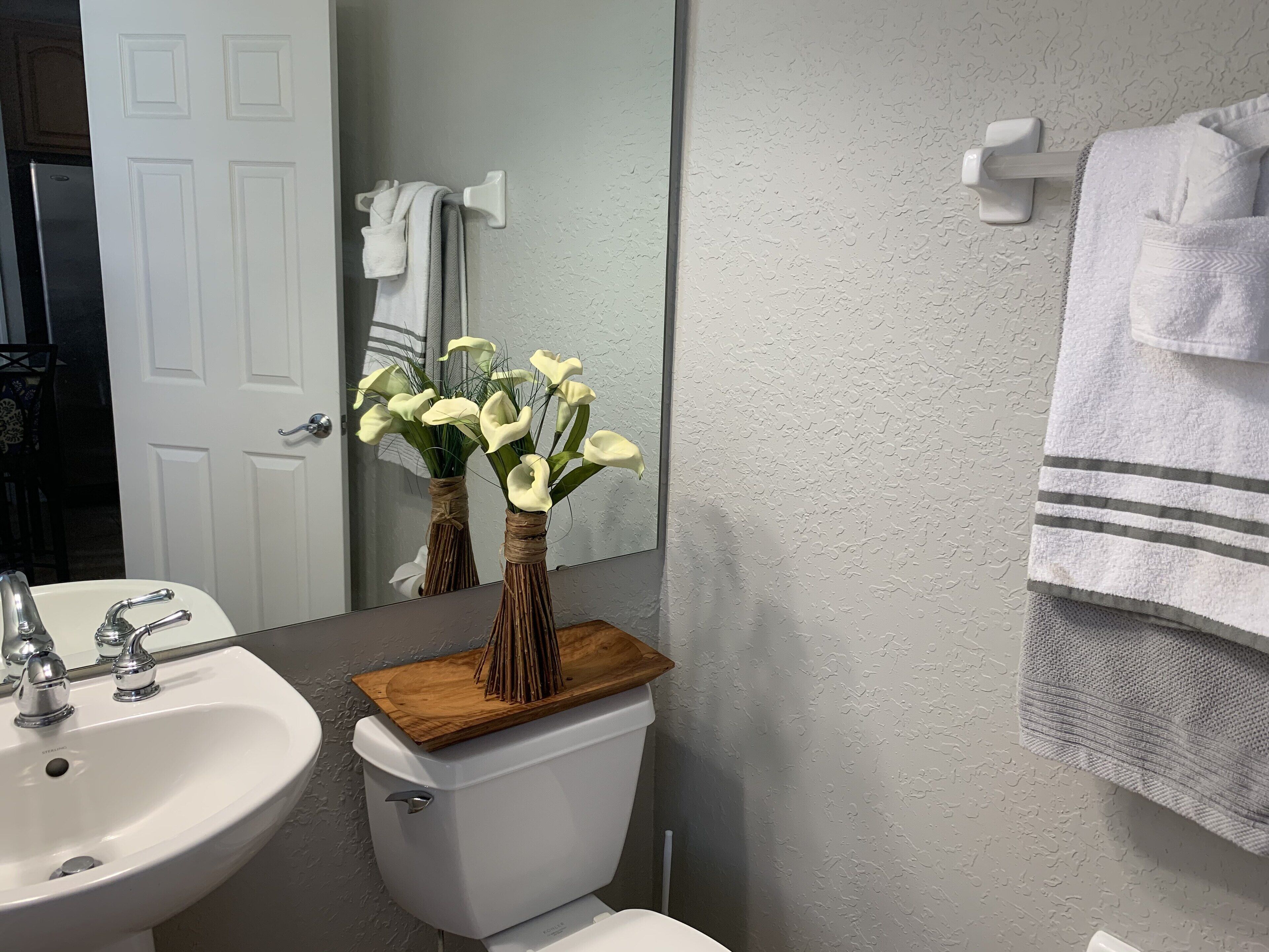 Ein Badezimmer mit einem weißen Waschbecken, einer Toilette und einem Spiegel. Weiße Handtücher hängen an einem Handtuchhalter.