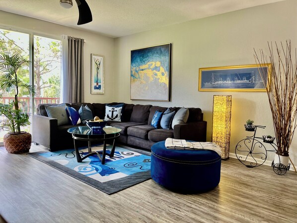 Een moderne woonkamer met een bank, poef, salontafel en decoratieve objecten.