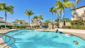 A swimming pool with lounge chairs and palm trees, surrounded by buildings. - Short/Long Term Fully Furnished Rental (Carlsbad)